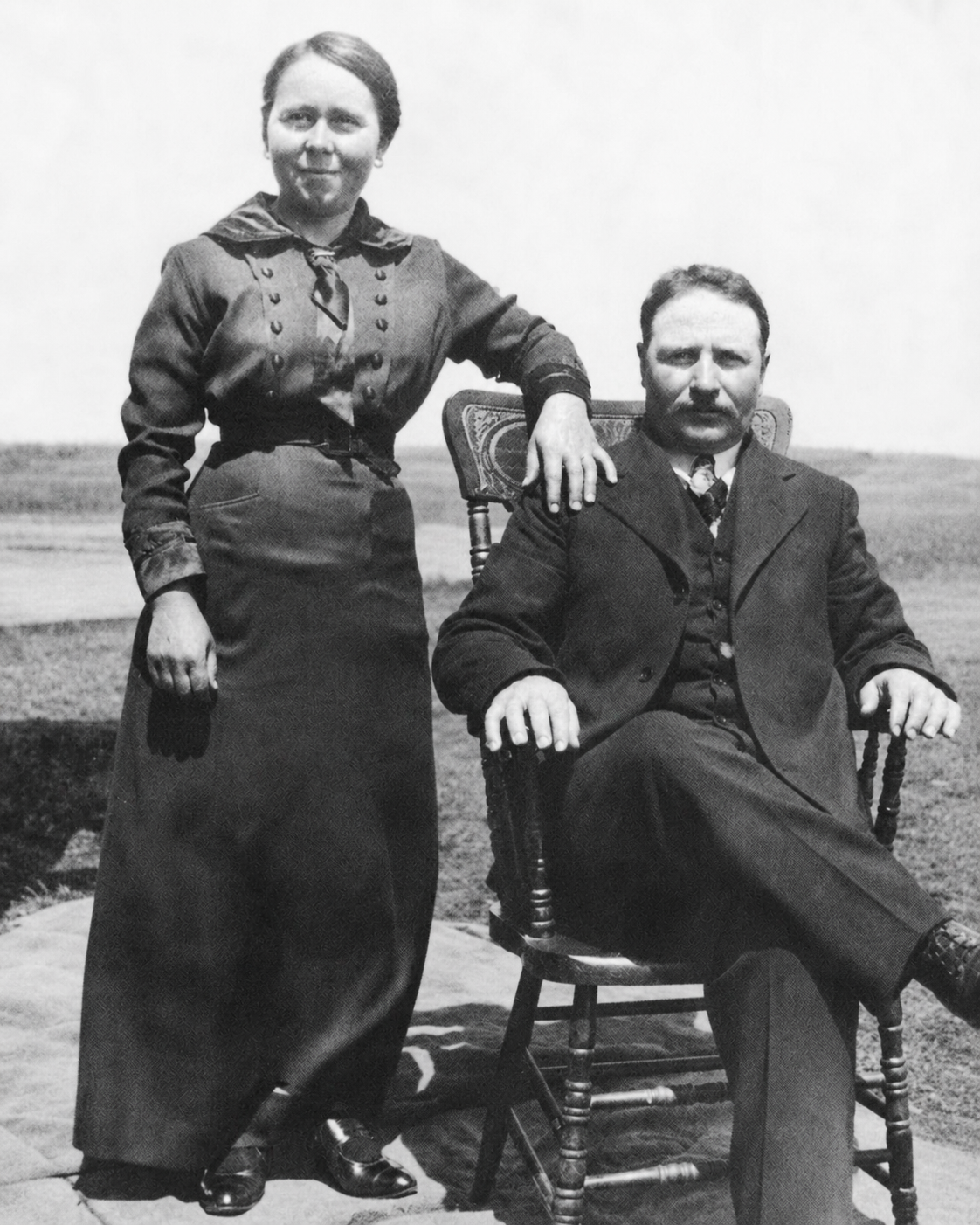 Maria Debreceni Daku standing beside Alexander Alex Daku, who is seated outdoors, about 1920.