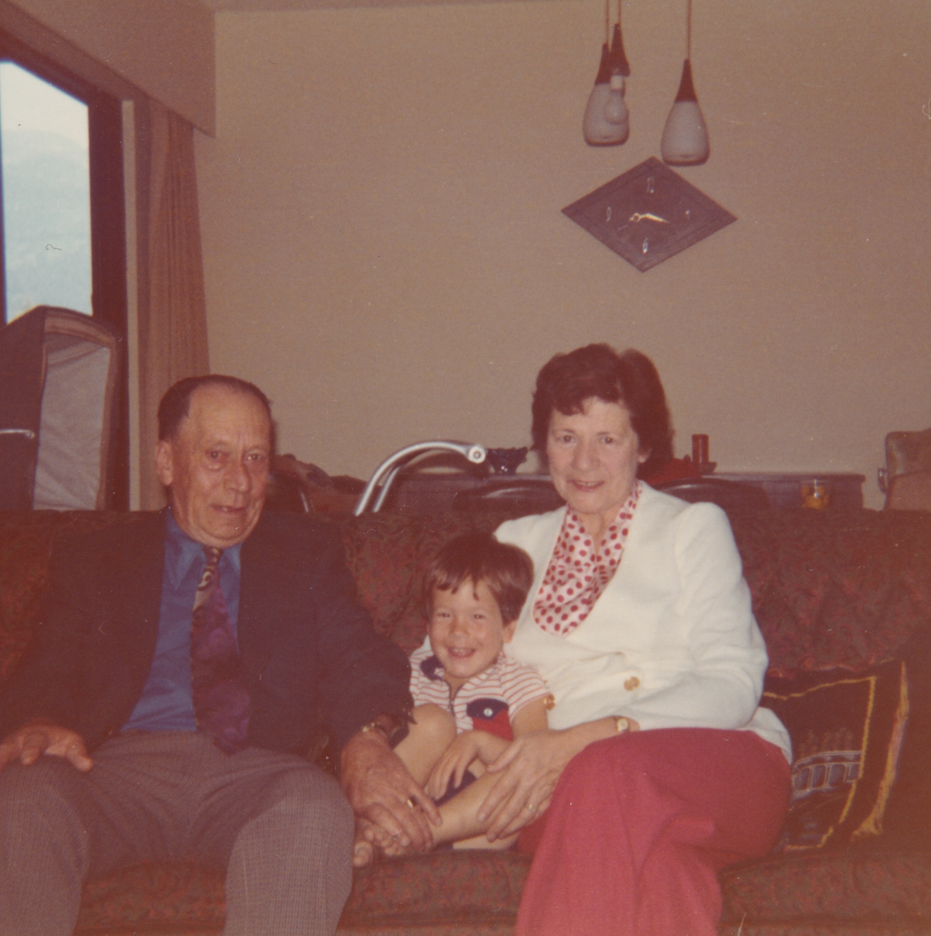 Color photograph of Lowell Simpson and Grace Davis Simpson seated on a couch with a young child between them.