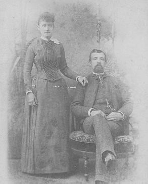 Studio portrait of Mahala Mitchell Ferguson standing beside Levi Ferguson, who is seated.